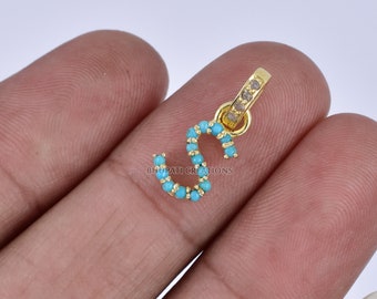 May include: Gold charm with the letter 'S' encrusted with turquoise blue stones and clear diamonds.  BHUPATI CREATIONS is printed on the charm.