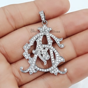May include: A silver pendant with a monogram design featuring the letters "A" and "S" set with clear cubic zirconia stones.