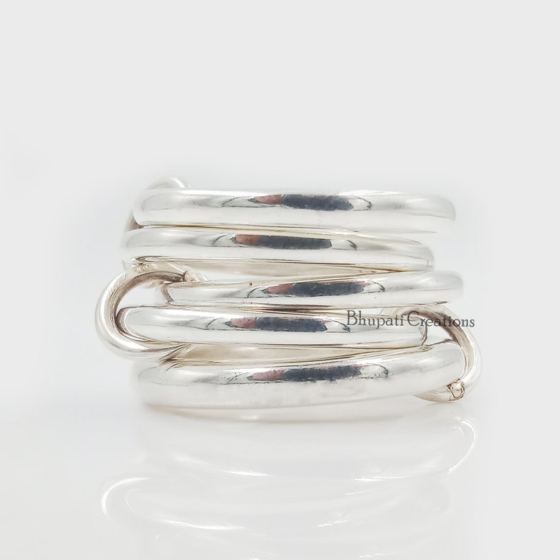 May include: Silver ring with multiple bands twisted together. The ring is made of polished silver and has a smooth, rounded surface.