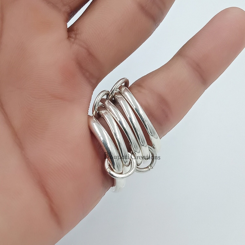 May include: A silver ring with multiple interlocking bands. The ring is worn on a finger.