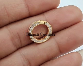 May include: A gold-colored, circular jewelry clasp with a hinged opening. The clasp is encrusted with small, clear gemstones around the outer edge. The text "Bhupati Creations" is printed on the clasp.