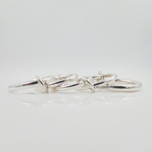 May include: Four silver rings interlocked together. The rings are smooth and shiny. The rings are arranged in a circle.