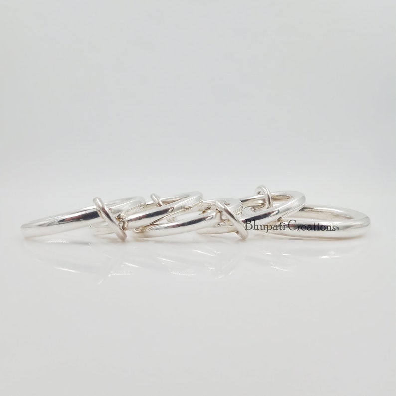 May include: Four silver rings interlocked together. The rings are smooth and shiny. The rings are arranged in a circle.