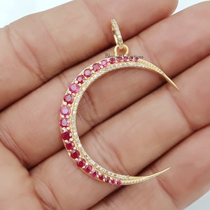 May include: A gold crescent moon pendant with a row of red ruby stones and a row of clear white stones around the edge.