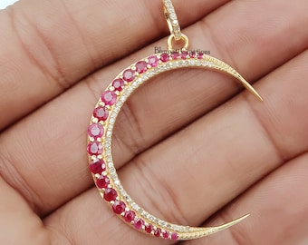 May include: A gold crescent moon pendant with a row of red ruby stones and a row of clear white stones around the edge.