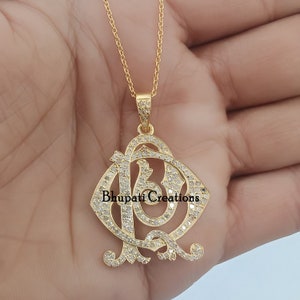 May include: A gold pendant necklace featuring a diamond-encrusted initial 'AD' design. The pendant is on a fine gold chain.