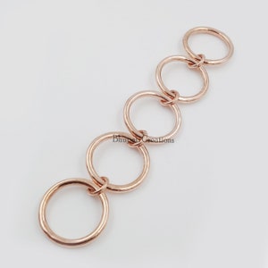 May include: A chain of five interlocking rose gold rings. The rings are all the same size and are connected to each other by a small loop.