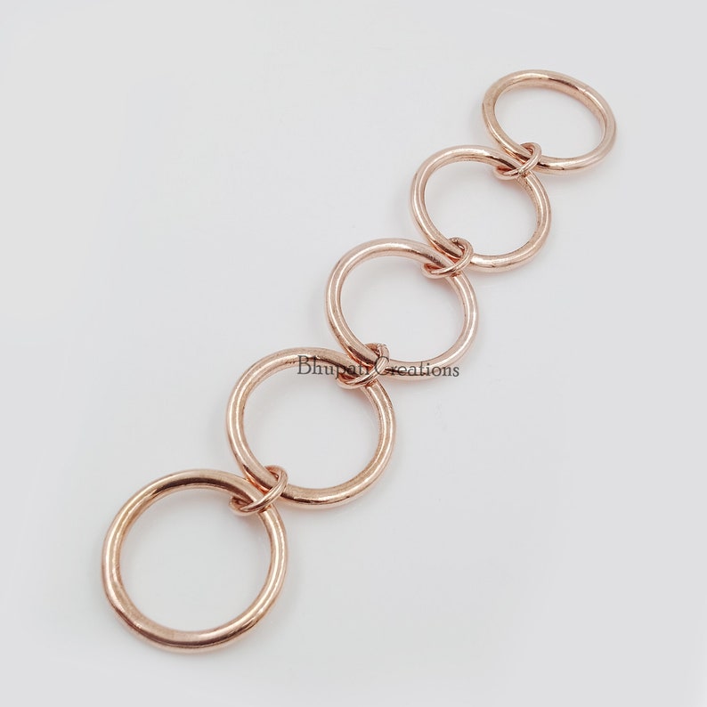 May include: A chain of five interlocking rose gold rings. The rings are all the same size and are connected to each other by a small loop.