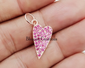 Könnte beinhalten: Ein herzförmiger Anhänger aus Roségold mit einer Pavé-Fassung aus rosa Zirkonia-Steinen. Der Anhänger hat eine Öse oben zum Anbringen an einer Halskette oder einem Armband.