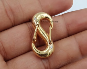 May include: Gold-toned metal clasp with two small clear gemstones. The clasp is shaped like an infinity symbol.