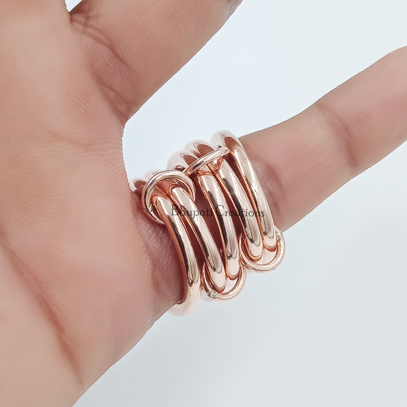 May include: A rose gold ring with multiple bands that are intertwined. The ring is worn on a finger.