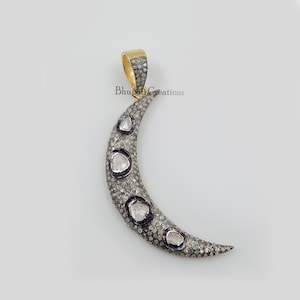 May include: A crescent moon pendant with a gold bail. The moon is encrusted with small, sparkling stones and features five larger, bezel-set diamonds. The pendant is designed to be worn as a necklace.