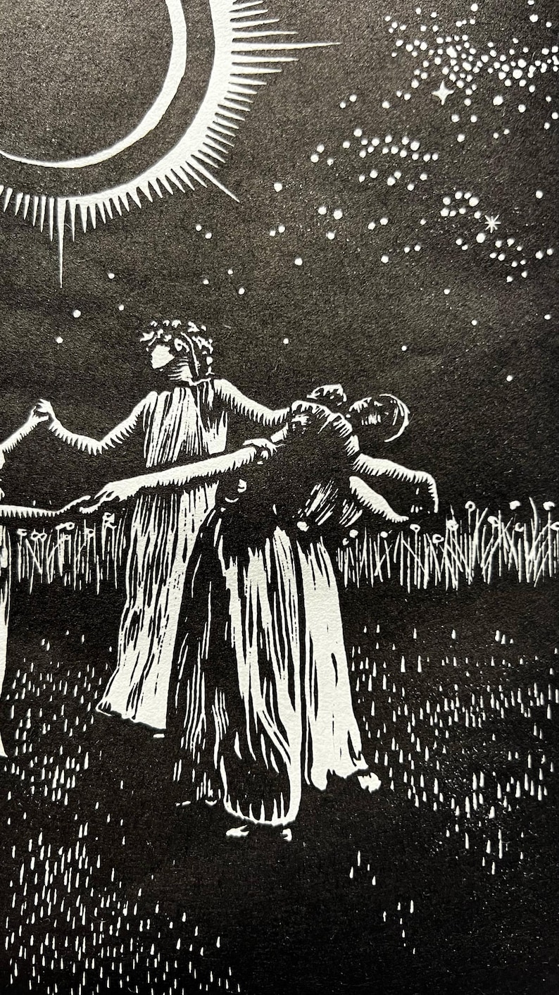 A detail shot of a Black and white art print depicting a celestial scene. A crescent moon with radiating lines is centered above 5 female figures in flowing robes, holding hands in a circle. The background is a starry night sky, with a field of tall grass in the foreground.