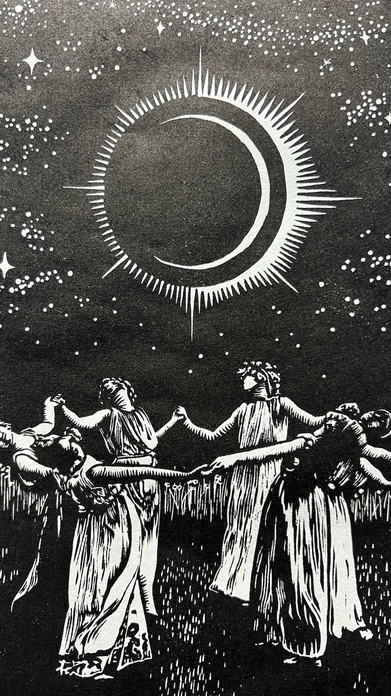 A detail shot of a Black and white art print depicting a celestial scene. A crescent moon with radiating lines is centered above 5 female figures in flowing robes, holding hands in a circle. The background is a starry night sky, with a field of tall grass in the foreground.