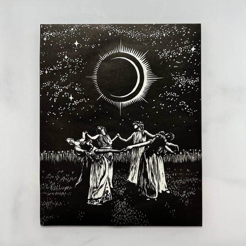 Black and white art print depicting a celestial scene. A crescent moon with radiating lines is centered above 5 female figures in flowing robes, holding hands in a circle. The background is a starry night sky, with a field of tall grass in the foreground.