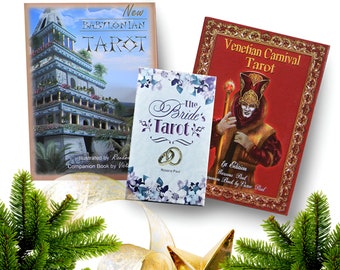 May include: Three different tarot decks: The Babylonian Tarot with a blue and gold cover, The Bride's Tarot with a white and purple cover, and the Venetian Carnival Tarot with a red and gold cover.