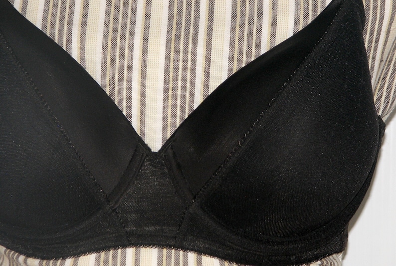 May include: A black bra with a smooth, seamless cup and a delicate lace trim. The bra has a V-shaped neckline and adjustable straps.