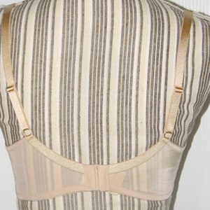 May include: A nude-colored bra with adjustable straps and a hook and eye closure in the back. The bra is made of a sheer, delicate fabric.
