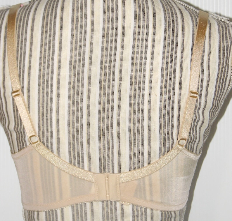 May include: A nude-colored bra with adjustable straps and a hook and eye closure in the back. The bra is made of a sheer, delicate fabric.