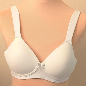 May include: A white bra with adjustable straps and a small bow detail at the center. The bra has a classic design with molded cups and a smooth, seamless appearance. The bra is displayed on a mannequin.