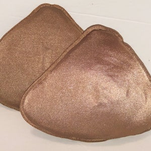 May include: Two brown triangle-shaped bra inserts. The inserts are made of a soft, smooth fabric and have a slightly textured surface.
