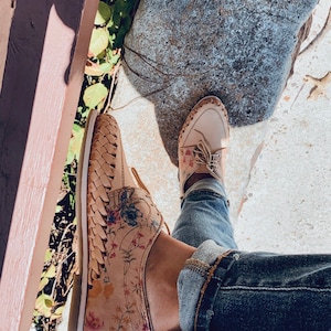 May include: A pair of floral patterned shoes with woven details. The shoes are worn with blue jeans.
