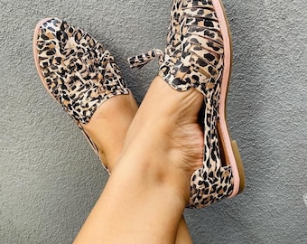 May include: A pair of brown and black leopard print sandals with a pink trim and a tassel detail.