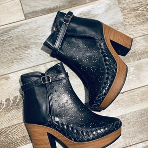 May include: A pair of black leather ankle boots with a woven wood platform sole and a buckle closure. The boots have a cutout design with small floral patterns.