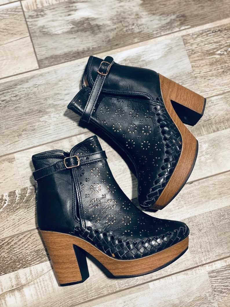 May include: A pair of black leather ankle boots with a woven wood platform sole and a buckle closure. The boots have a cutout design with small floral patterns.