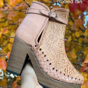May include: Tan leather ankle boots with a woven platform sole and a floral tooled design. The boots have a buckle closure and a block heel. The text "Tooled Tan" is visible in the image.