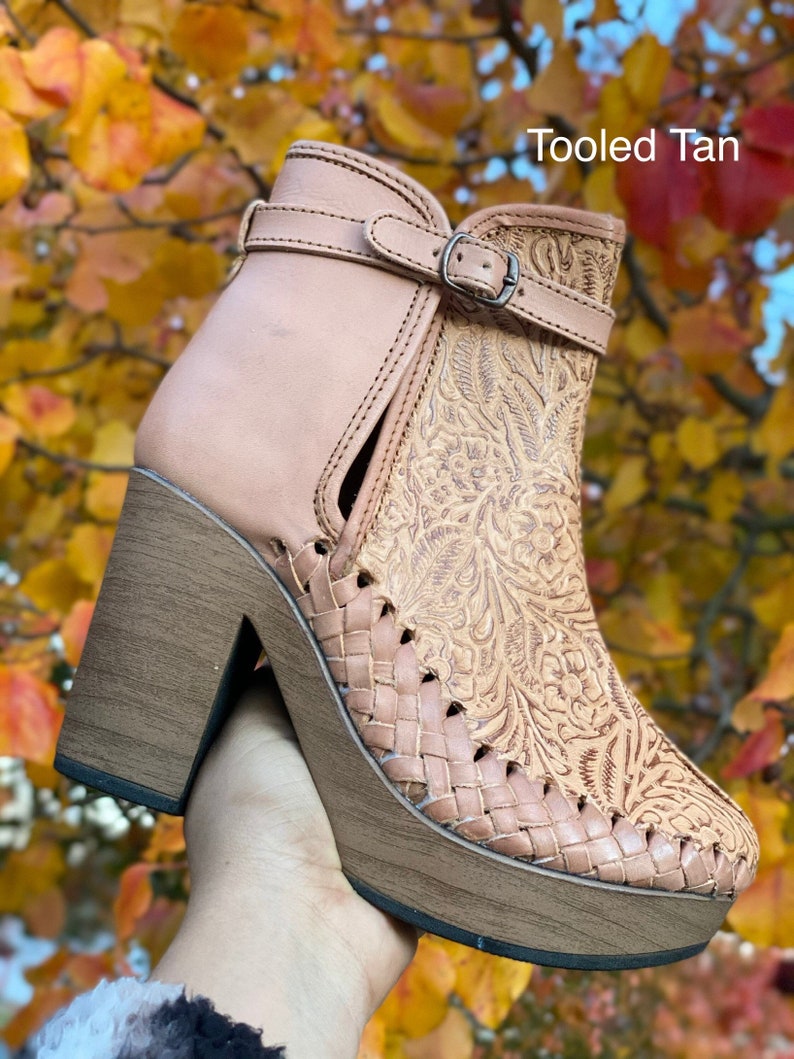 May include: Tan leather ankle boots with a woven platform sole and a floral tooled design. The boots have a buckle closure and a block heel. The text "Tooled Tan" is visible in the image.