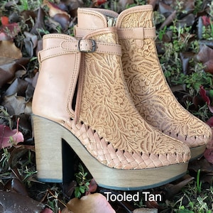 May include: Tan leather ankle boots with a floral embossed design and a woven platform heel. The boots have a buckle closure and a side zipper. The text "Tooled Tan" is visible in the image.