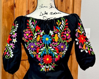 May include: Black embroidered blouse with colorful floral design. The blouse has a scoop neck and 3/4 sleeves. The text "Black SMALL" is visible in the image.