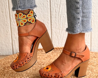 Könnte beinhalten: Braune Lederplattform-Heels mit einem Sonnenblumen-Stickmuster. Die Absätze haben einen dicken Blockabsatz und einen Knöchelriemen mit einer Schnalle.