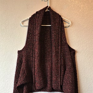 May include: A maroon sleeveless cardigan with a draped neckline and a slightly asymmetrical hem.