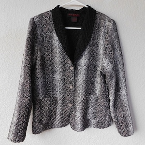 May include: A black and white patterned cardigan with a black knit collar and button closure. The label "Ruth Colection" is visible on the collar.