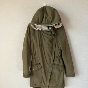 May include: A long, green hooded jacket with a drawstring waist and a fleece lining. The jacket has two large pockets on the front and a zipper closure.
