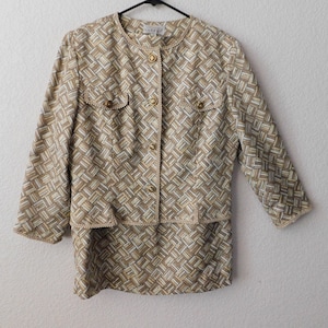 May include: A beige and brown patterned jacket with gold buttons and a matching skirt. The jacket has a round neckline and three-quarter sleeves. The skirt is knee-length.