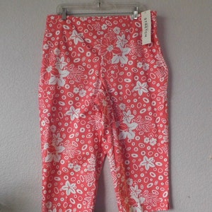 May include: A pair of coral-colored capri pants with a white floral print and a white tag that says "STRETCH".