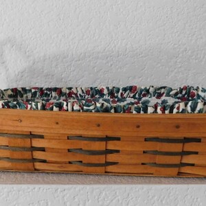 May include: A rectangular woven basket with leather handles. The basket is lined with a white fabric with a green and red holly berry pattern.