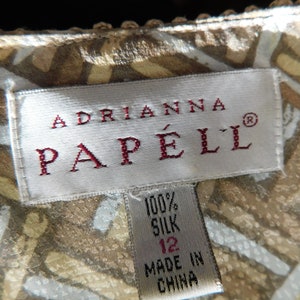 May include: A white tag with red text that reads "Adrianna Papell&reg;" and a smaller white tag with black text that reads "100% Silk 12 Made in China".