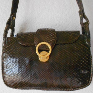 May include: A dark brown snakeskin handbag with a gold-toned clasp and a shoulder strap.