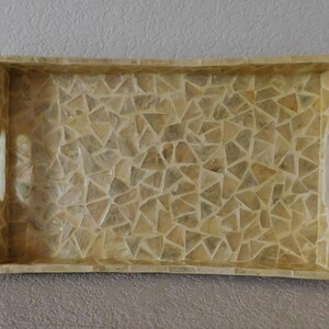 May include: Rectangular decorative tray with a mosaic pattern of small, irregularly shaped pieces in shades of beige and cream. The tray has a raised border and cut-out handles on each side.