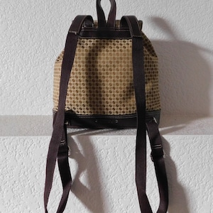 May include: A brown and beige patterned backpack with adjustable straps. The backpack has a drawstring closure and a brown leather trim.