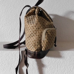 May include: A brown and beige patterned backpack with a brown leather bottom and a zippered pocket on the side.