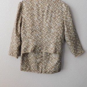 May include: A beige and white patterned jacket with a long sleeve and a slightly cropped length. The jacket has a geometric pattern and a subtle sheen.