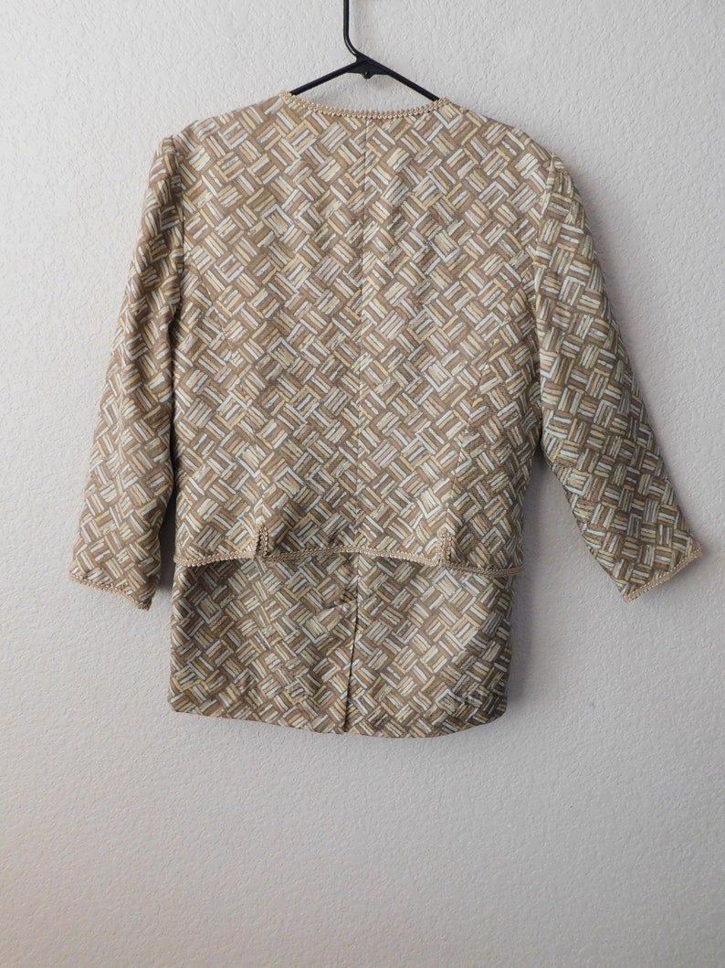 May include: A beige and white patterned jacket with a long sleeve and a slightly cropped length. The jacket has a geometric pattern and a subtle sheen.