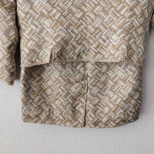 May include: A brown and white patterned jacket with a brown trim around the edges. The jacket has a geometric pattern and a button closure.