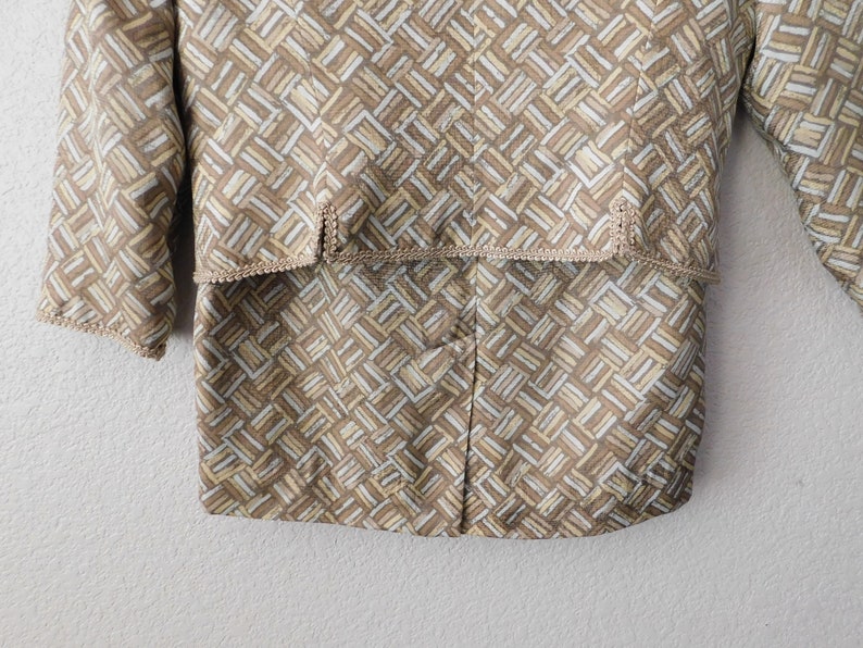 May include: A brown and white patterned jacket with a brown trim around the edges. The jacket has a geometric pattern and a button closure.