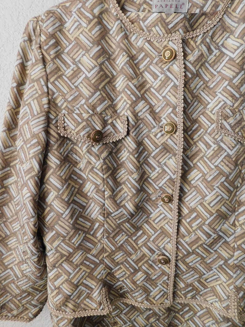 May include: A brown and white patterned blazer with gold buttons and a decorative trim. The label reads "Adrienne Vittadini PAPEL".